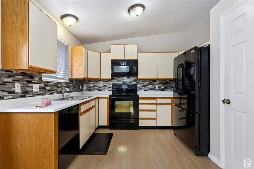 Kitchen with black appliances, sink, vaulted ceiling, backsplash, and light hardwood / wood-style floors