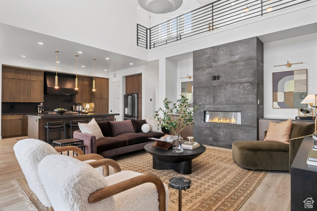 Living room featuring a tiled fireplace, a towering ceiling, and light hardwood / wood-style floors