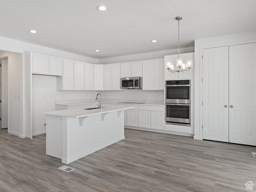 Kitchen with a chandelier, pendant lighting, a center island with sink, appliances with stainless steel finishes, and light hardwood / wood-style flooring
