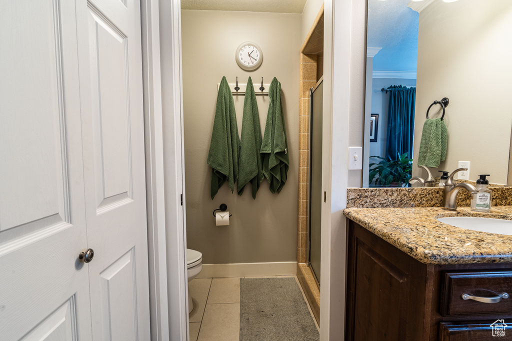 Bathroom with vanity, a shower with door, toilet, tile floors, and crown molding