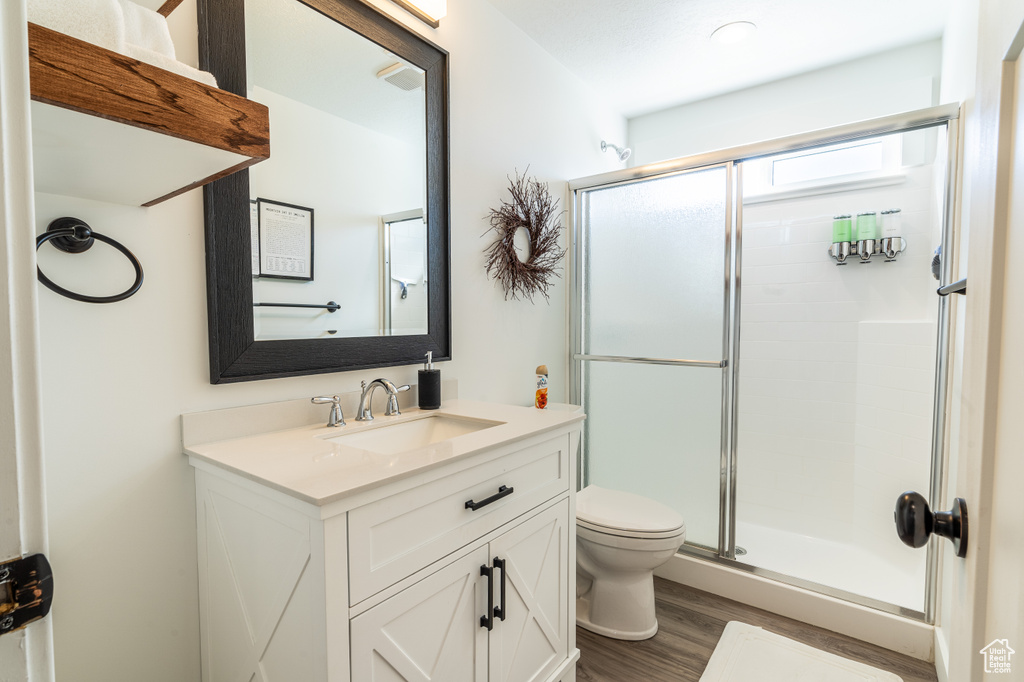 Bathroom with wood-type flooring, vanity with extensive cabinet space, toilet, and a shower with shower door
