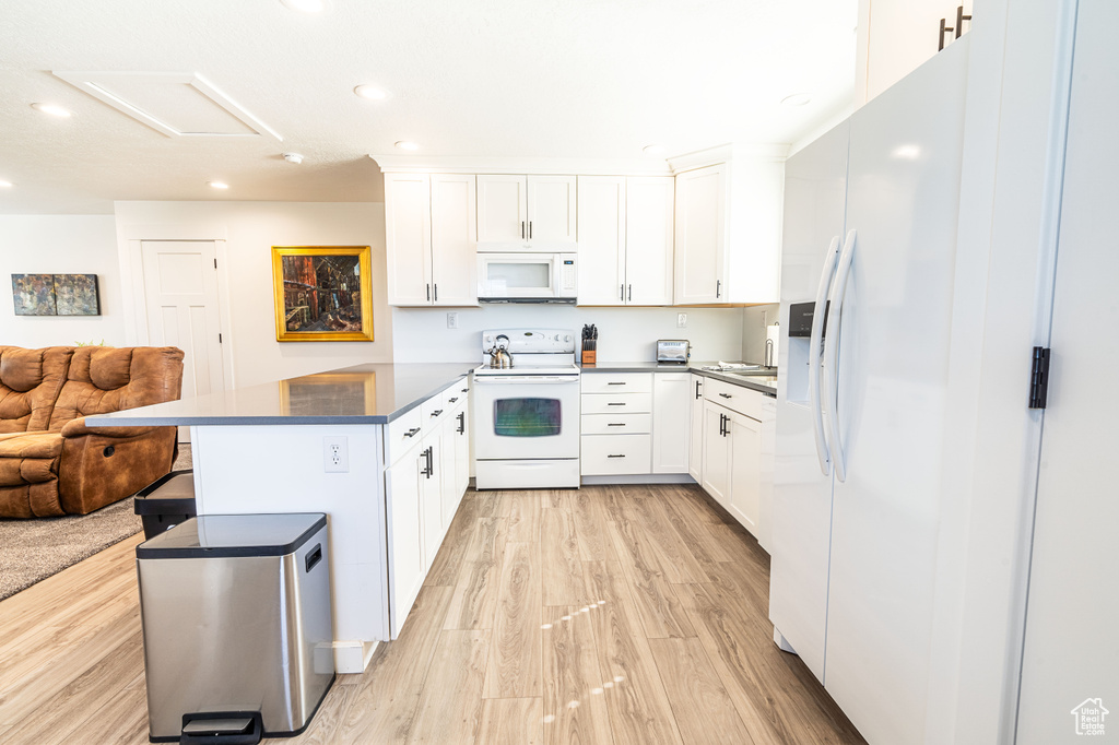 Kitchen with white cabinetry, white appliances, a breakfast bar area, and light hardwood / wood-style flooring