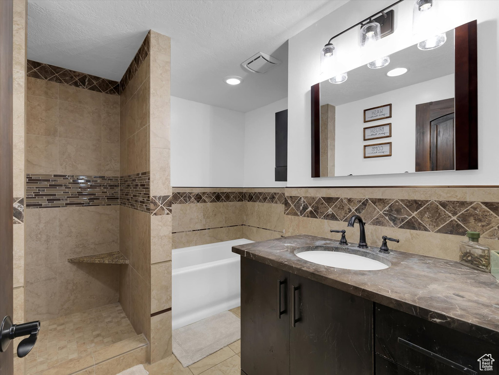 Bathroom with tile flooring, a bath to relax in, vanity with extensive cabinet space, and a textured ceiling