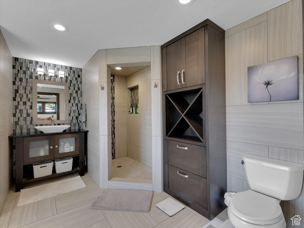 Bathroom with tiled shower, tile walls, vanity, tile flooring, and toilet