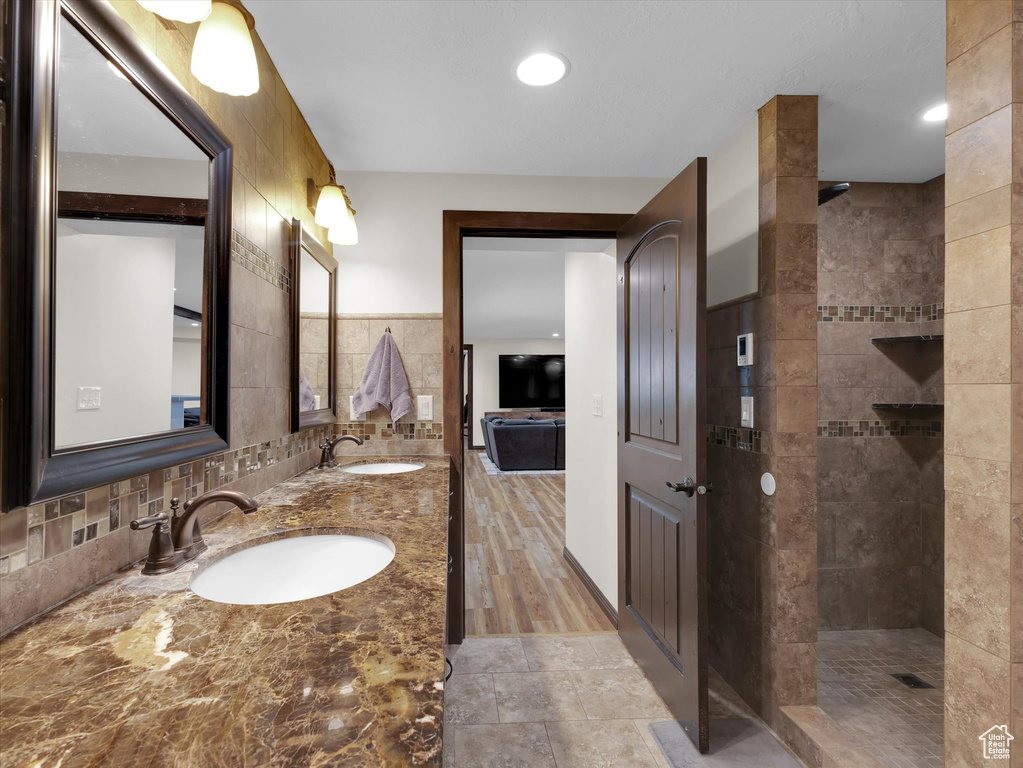 Bathroom featuring tile walls, dual sinks, oversized vanity, backsplash, and a tile shower