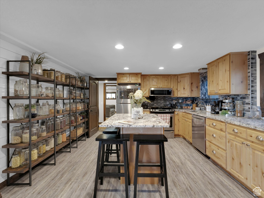 Kitchen with appliances with stainless steel finishes, light stone countertops, a kitchen island, and light hardwood / wood-style floors