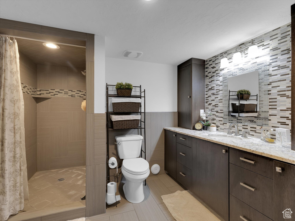 Bathroom featuring curtained shower, vanity, backsplash, tile flooring, and toilet