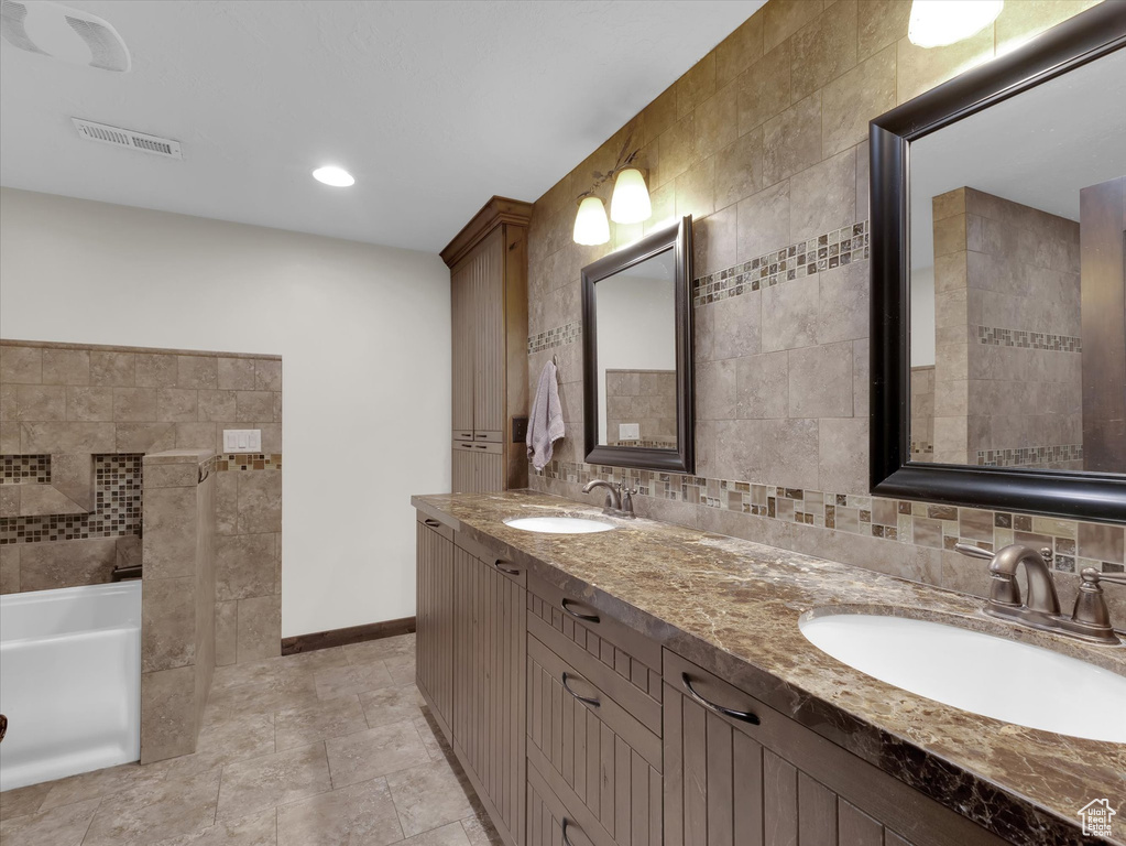 Bathroom featuring tile walls, a washtub, double vanity, tasteful backsplash, and tile floors