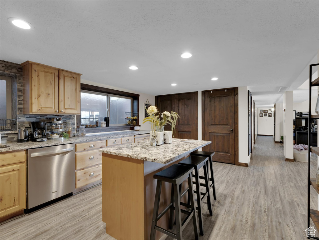 Kitchen featuring light hardwood / wood-style flooring, backsplash, a breakfast bar area, a kitchen island, and dishwasher
