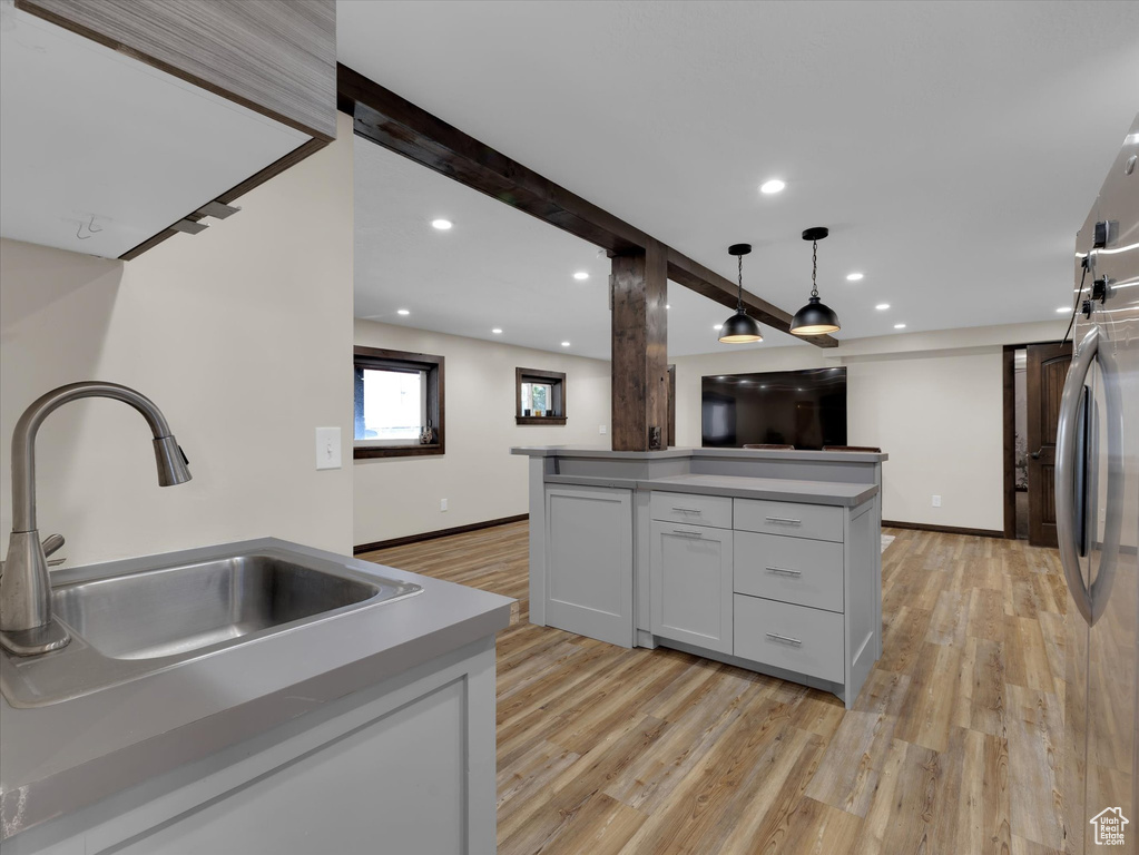 Kitchen with hanging light fixtures, white cabinets, light wood-type flooring, beam ceiling, and sink