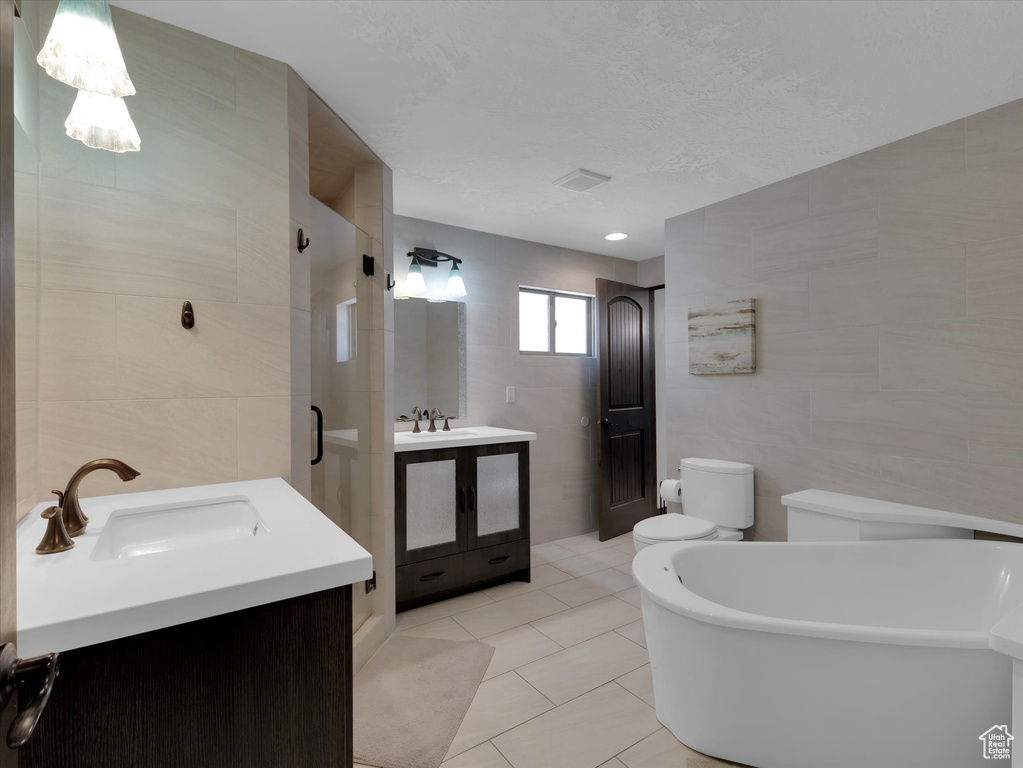 Full bathroom featuring tile walls, shower with separate bathtub, toilet, tile floors, and vanity