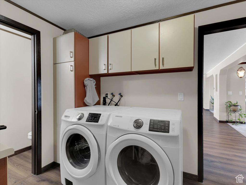 Washroom featuring wood-type flooring, washer hookup, washing machine and clothes dryer, cabinets, and a textured ceiling