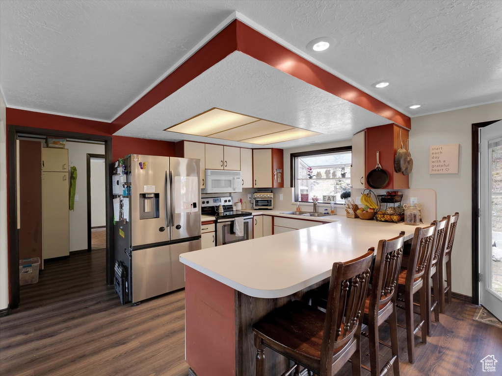 Kitchen featuring a textured ceiling, dark hardwood / wood-style flooring, stainless steel appliances, kitchen peninsula, and a kitchen breakfast bar