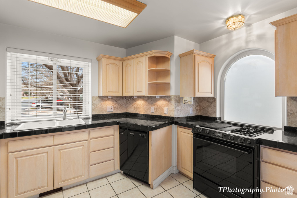 Kitchen featuring gas range oven, light tile floors, light brown cabinetry, and tasteful backsplash