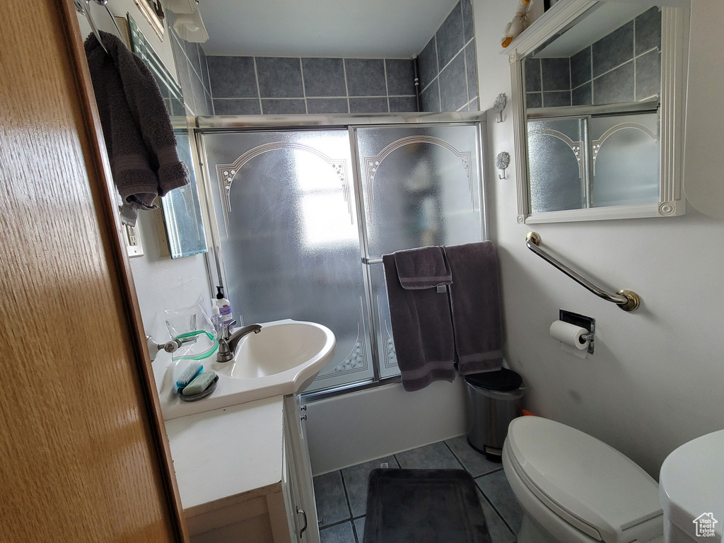 Full bathroom featuring combined bath / shower with glass door, toilet, tile floors, and sink