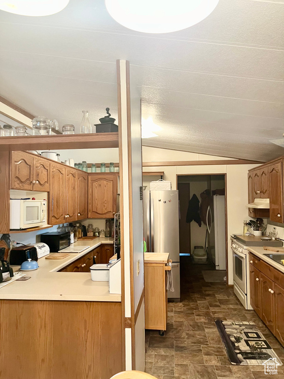 Kitchen featuring stainless steel fridge, lofted ceiling, electric range oven, and dark tile flooring