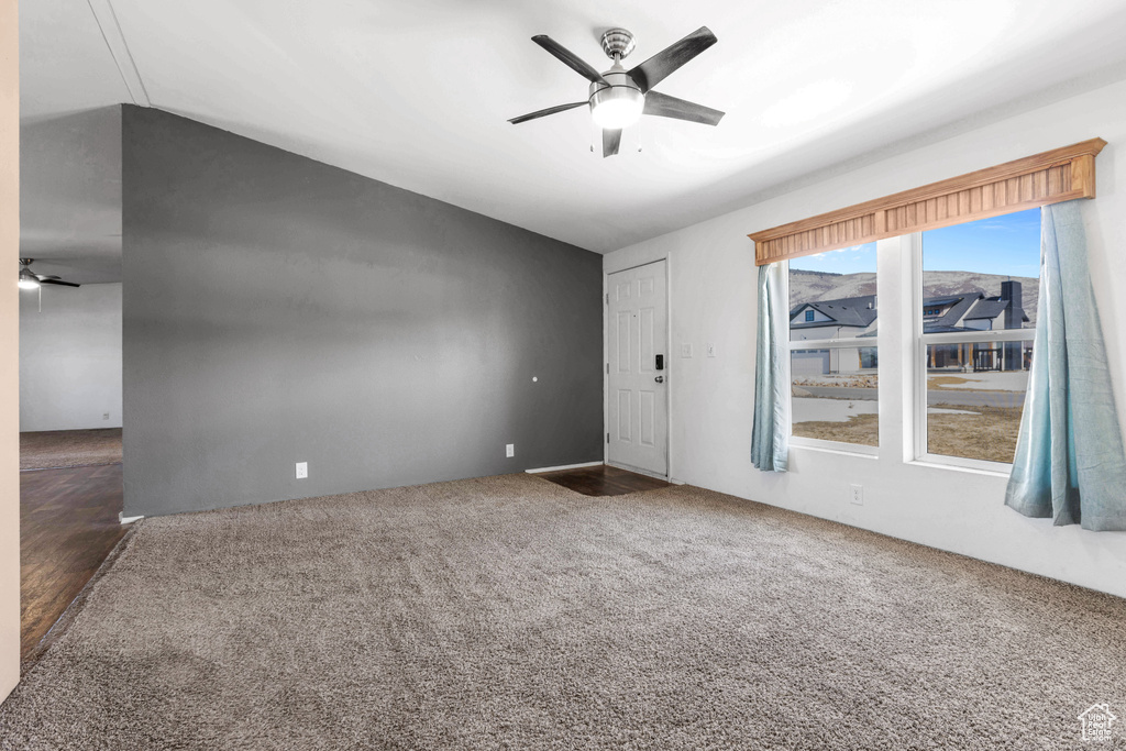 Spare room featuring dark colored carpet, vaulted ceiling, ceiling fan, and plenty of natural light