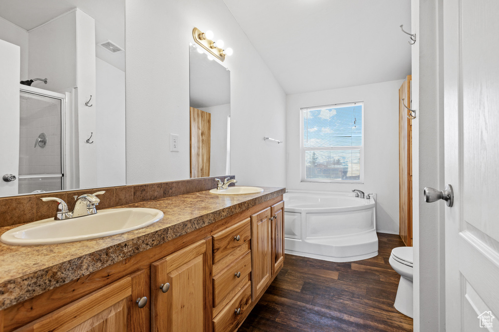 Full bathroom featuring hardwood / wood-style floors, independent shower and bath, lofted ceiling, toilet, and double vanity