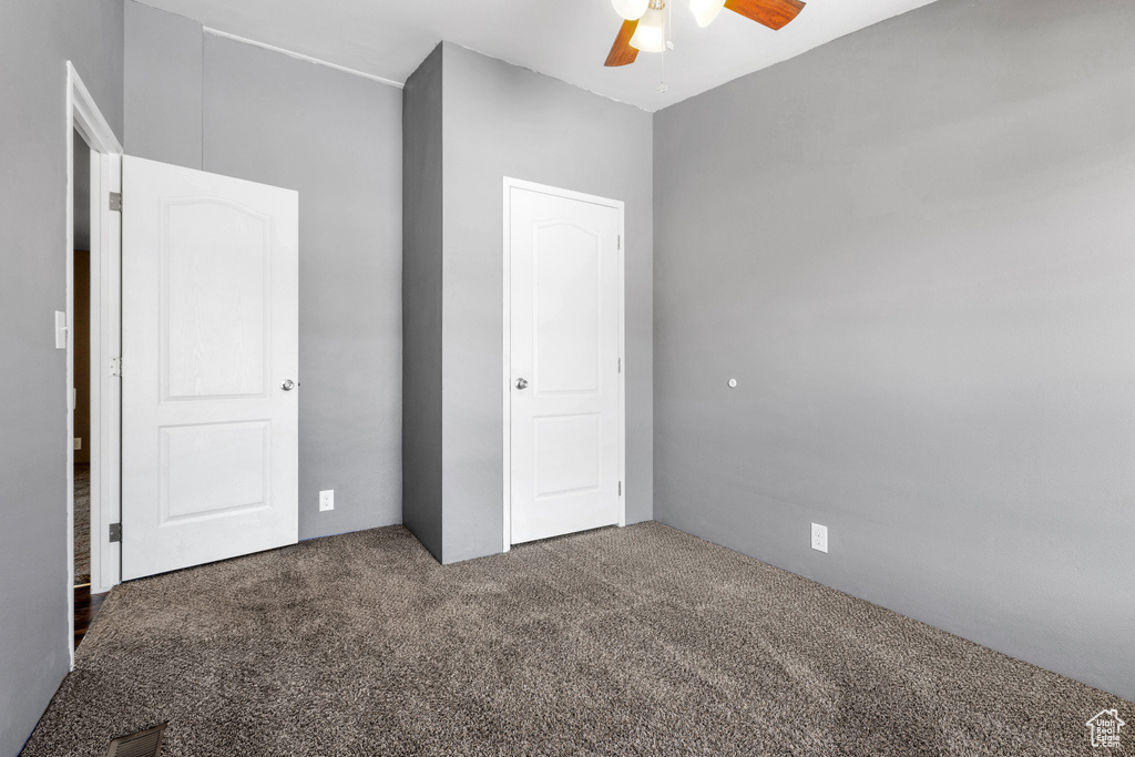 Unfurnished bedroom with dark carpet and ceiling fan