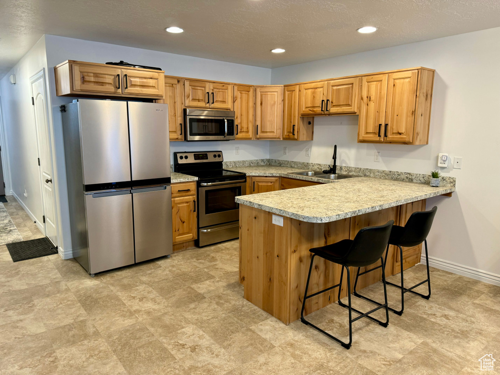 Kitchen featuring sink, stainless steel appliances, light tile flooring, and a breakfast bar