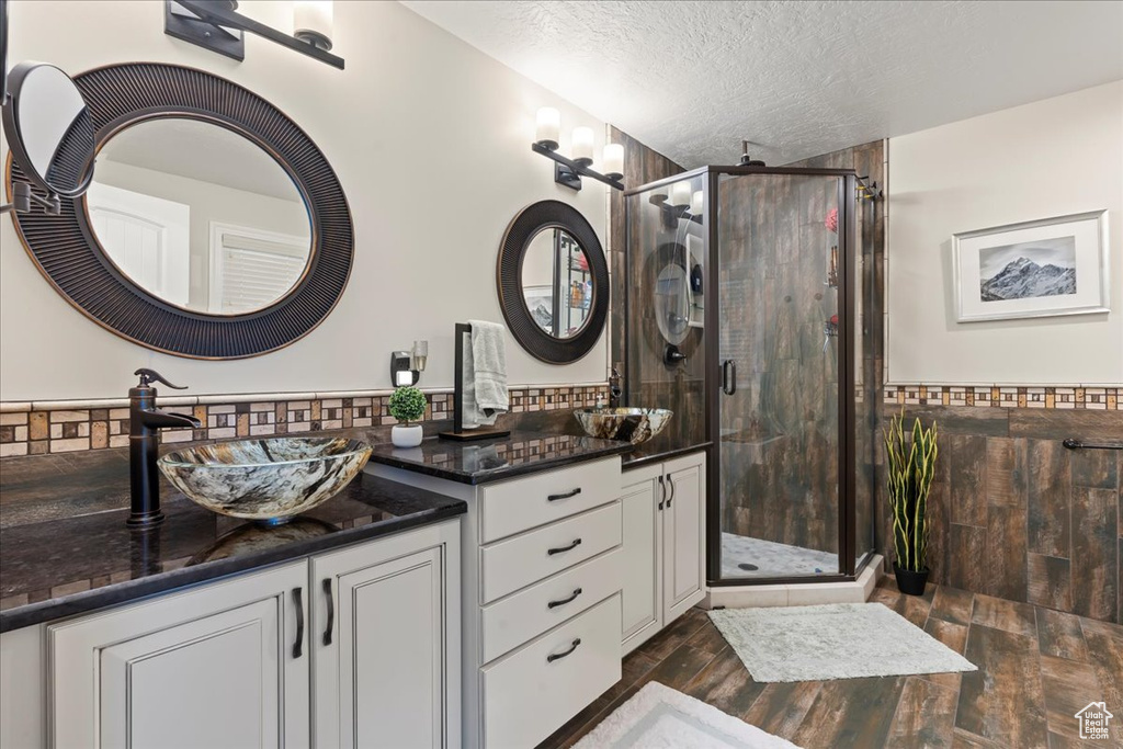 Bathroom featuring double vanity, a shower with door, and a textured ceiling