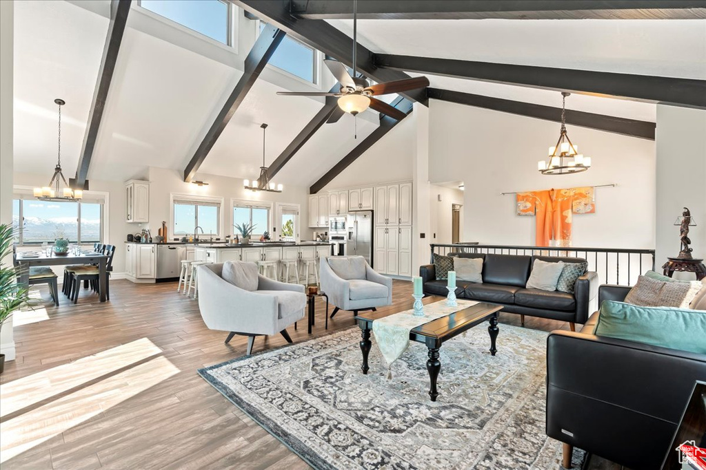 Living room with ceiling fan with notable chandelier, beamed ceiling, light hardwood / wood-style floors, and high vaulted ceiling