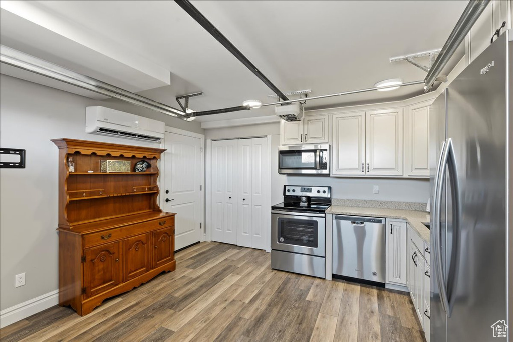 Kitchen with light hardwood / wood-style flooring, white cabinets, stainless steel appliances, and a wall mounted AC