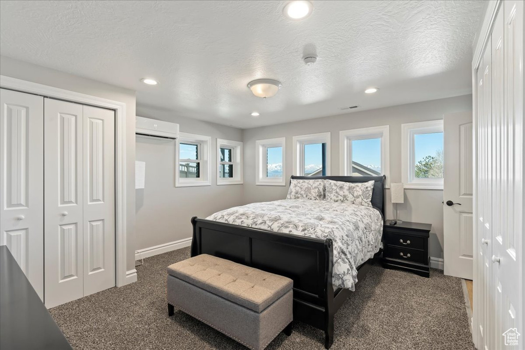 Bedroom with a wall unit AC, a textured ceiling, multiple closets, and dark carpet
