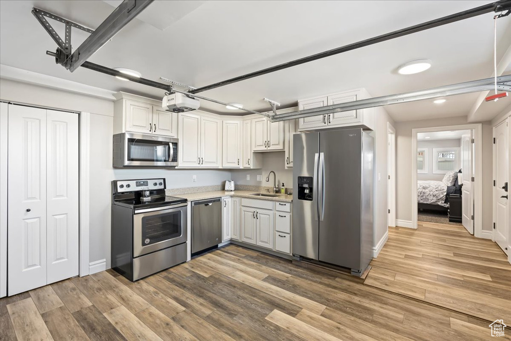 Kitchen with white cabinets, hardwood / wood-style flooring, stainless steel appliances, and sink
