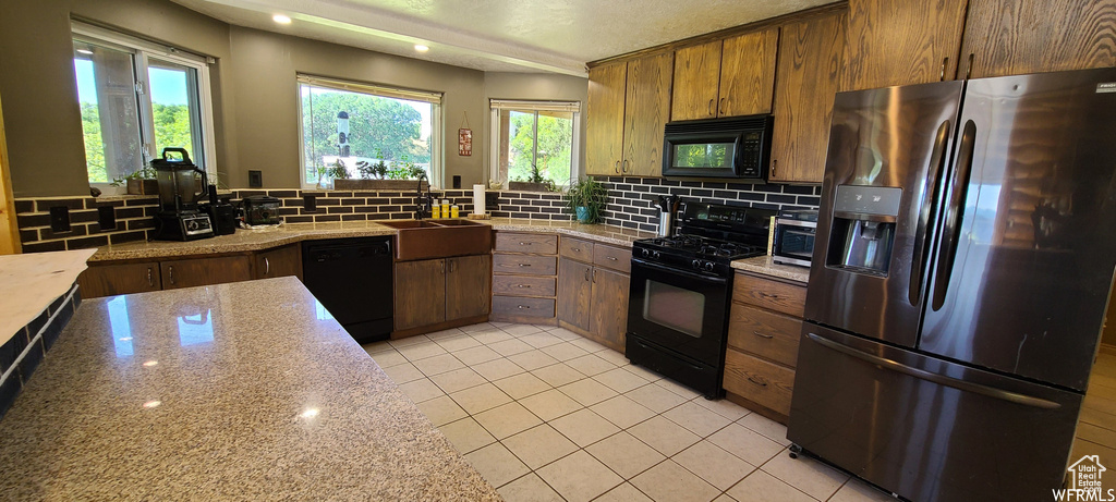 Kitchen with black appliances, tasteful backsplash, sink, and light stone countertops