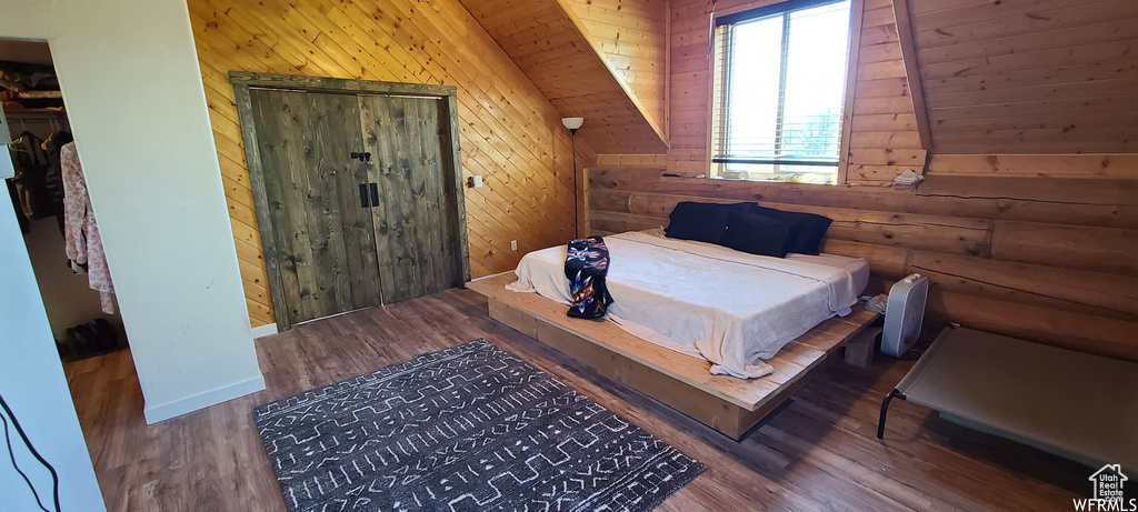 Bedroom featuring lofted ceiling, wooden walls, a closet, and dark wood-type flooring