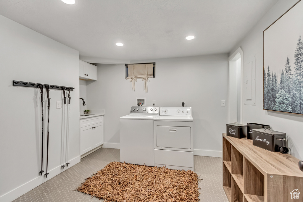 Washroom with light tile flooring, washing machine and clothes dryer, cabinets, and sink