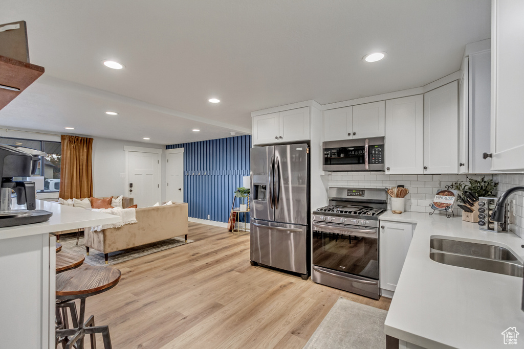 Kitchen with white cabinets, stainless steel appliances, sink, and light hardwood / wood-style flooring
