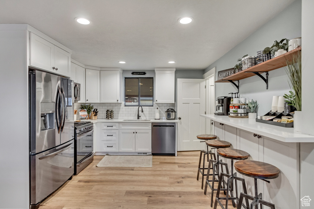 Kitchen featuring appliances with stainless steel finishes, sink, white cabinets, and light hardwood / wood-style flooring