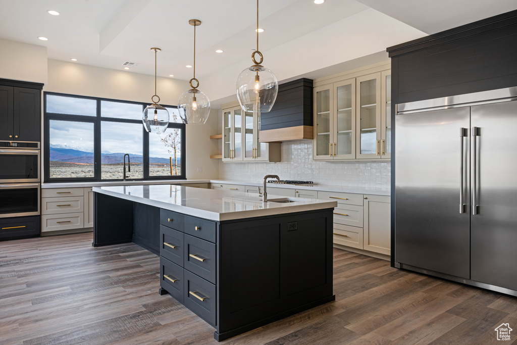 Kitchen featuring appliances with stainless steel finishes, white cabinets, a kitchen island with sink, dark hardwood / wood-style flooring, and decorative light fixtures