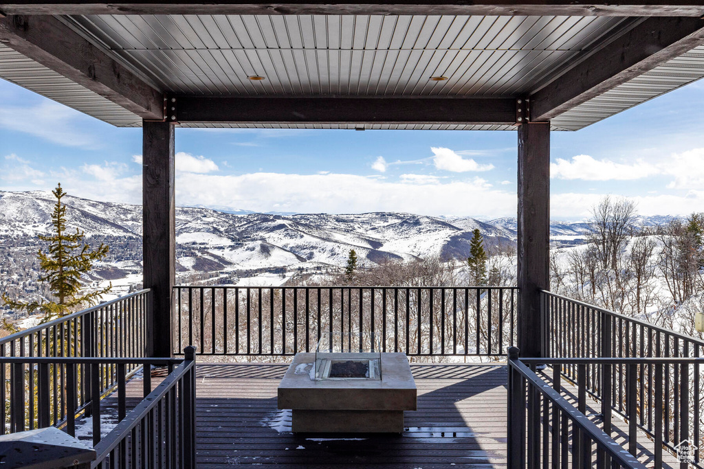 Snow covered deck featuring a mountain view and an outdoor fire pit