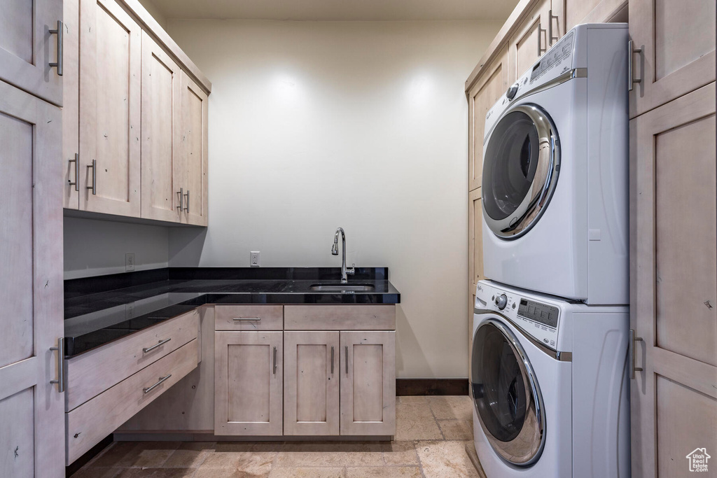 Washroom featuring stacked washer and dryer, light tile floors, cabinets, and sink