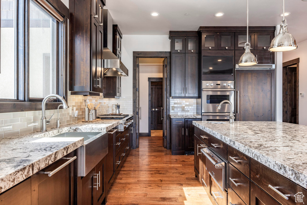 Kitchen featuring hardwood / wood-style flooring, backsplash, light stone counters, dark brown cabinets, and pendant lighting
