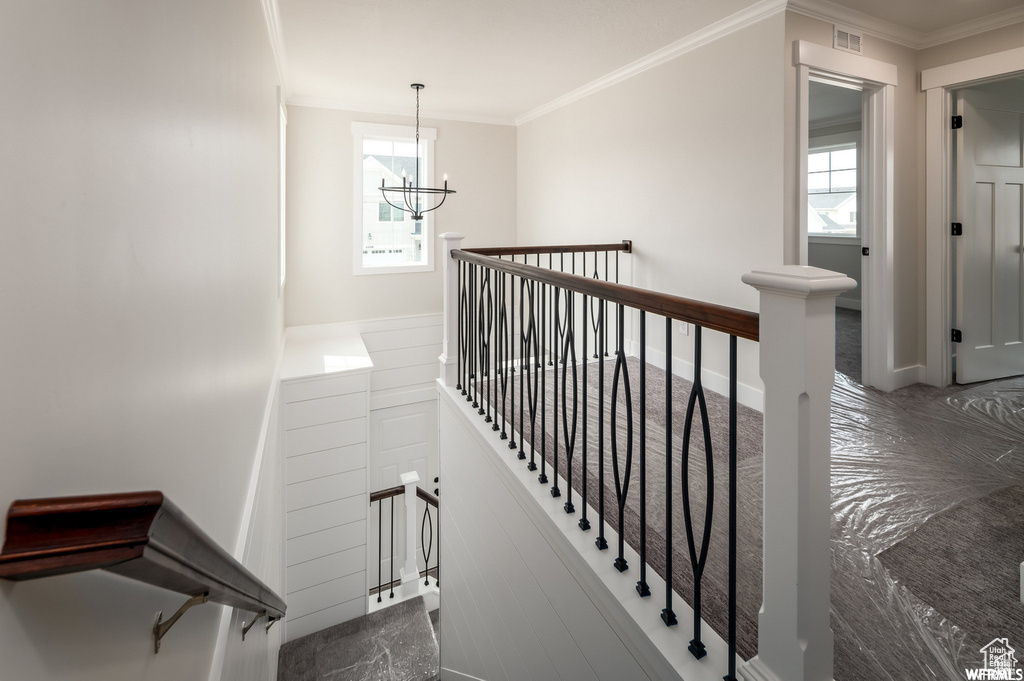Stairs with crown molding, a notable chandelier, and a healthy amount of sunlight