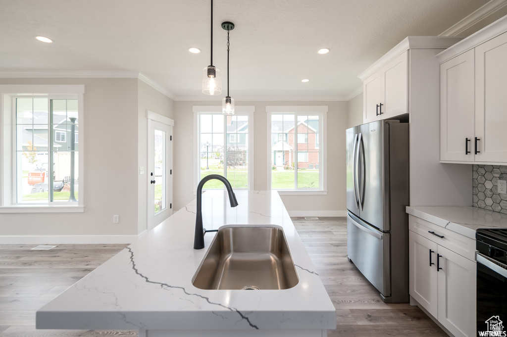 Kitchen featuring sink, stainless steel fridge, a kitchen island with sink, decorative light fixtures, and backsplash