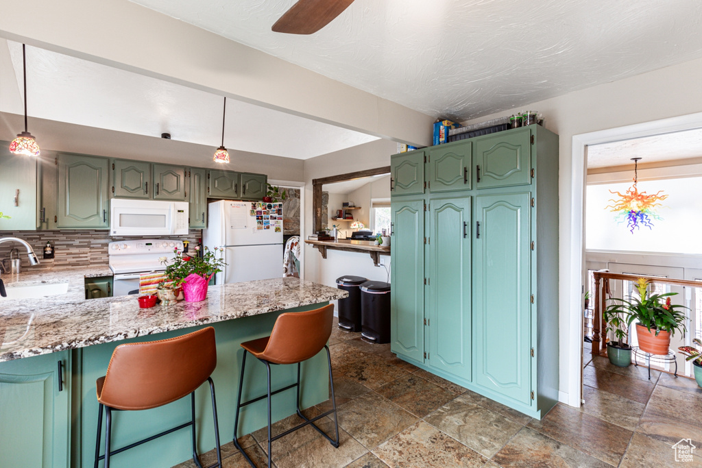 Kitchen with backsplash, ceiling fan, white appliances, hanging light fixtures, and dark tile flooring