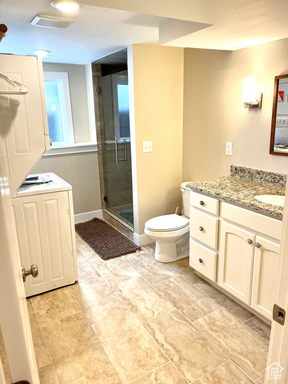 Bathroom featuring a shower with shower door, vanity, toilet, stacked washer / dryer, and tile flooring