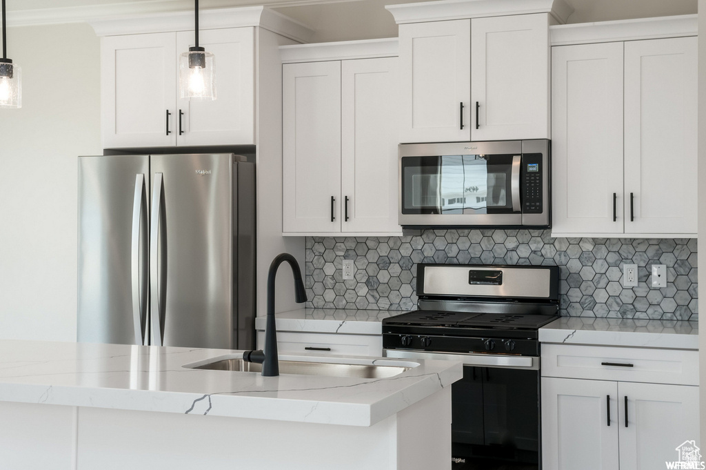 Kitchen featuring white cabinets, appliances with stainless steel finishes, backsplash, and decorative light fixtures