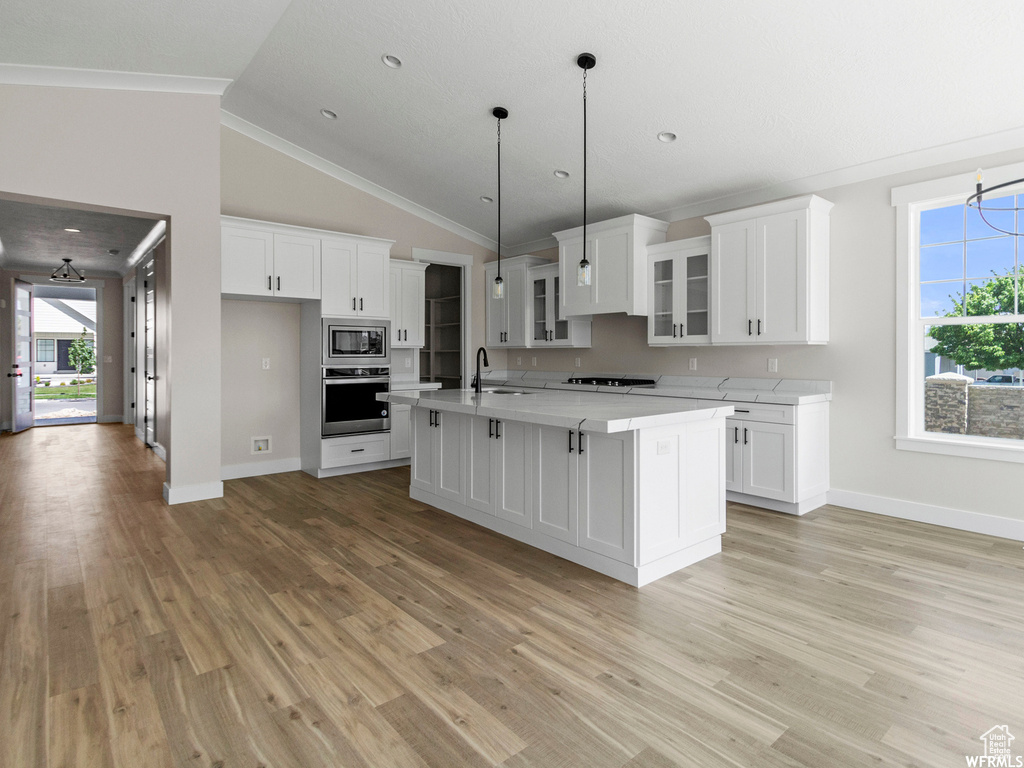 Kitchen featuring appliances with stainless steel finishes, ornamental molding, a kitchen island with sink, sink, and light wood-type flooring