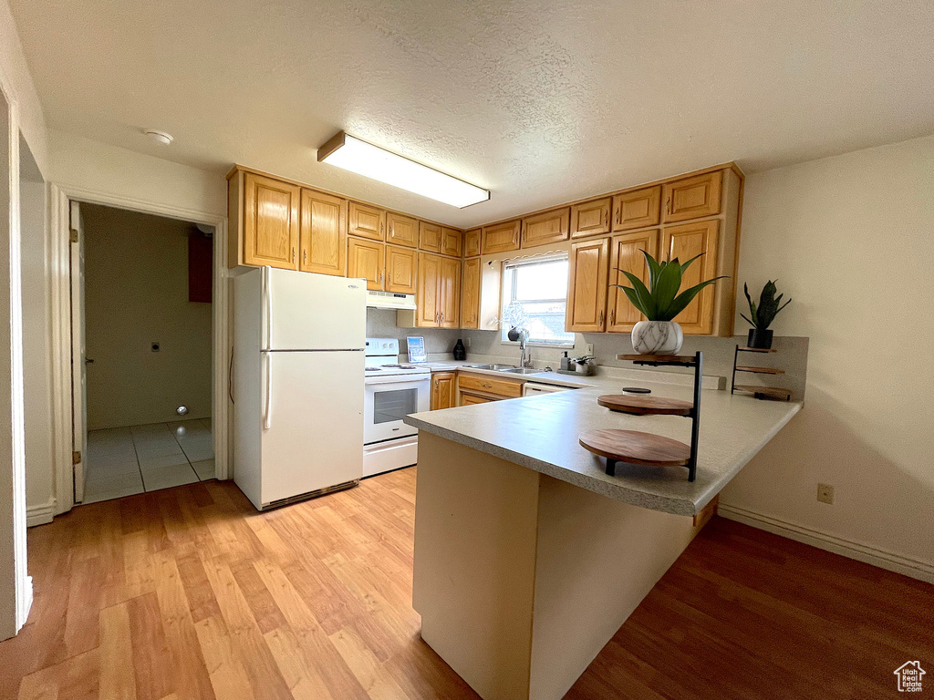 Kitchen with light hardwood / wood-style flooring, kitchen peninsula, and white appliances