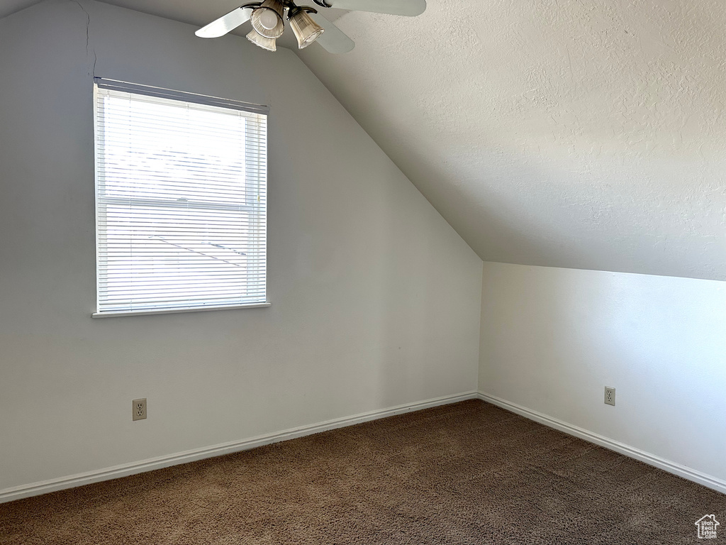 Additional living space featuring dark colored carpet, a textured ceiling, vaulted ceiling, and ceiling fan