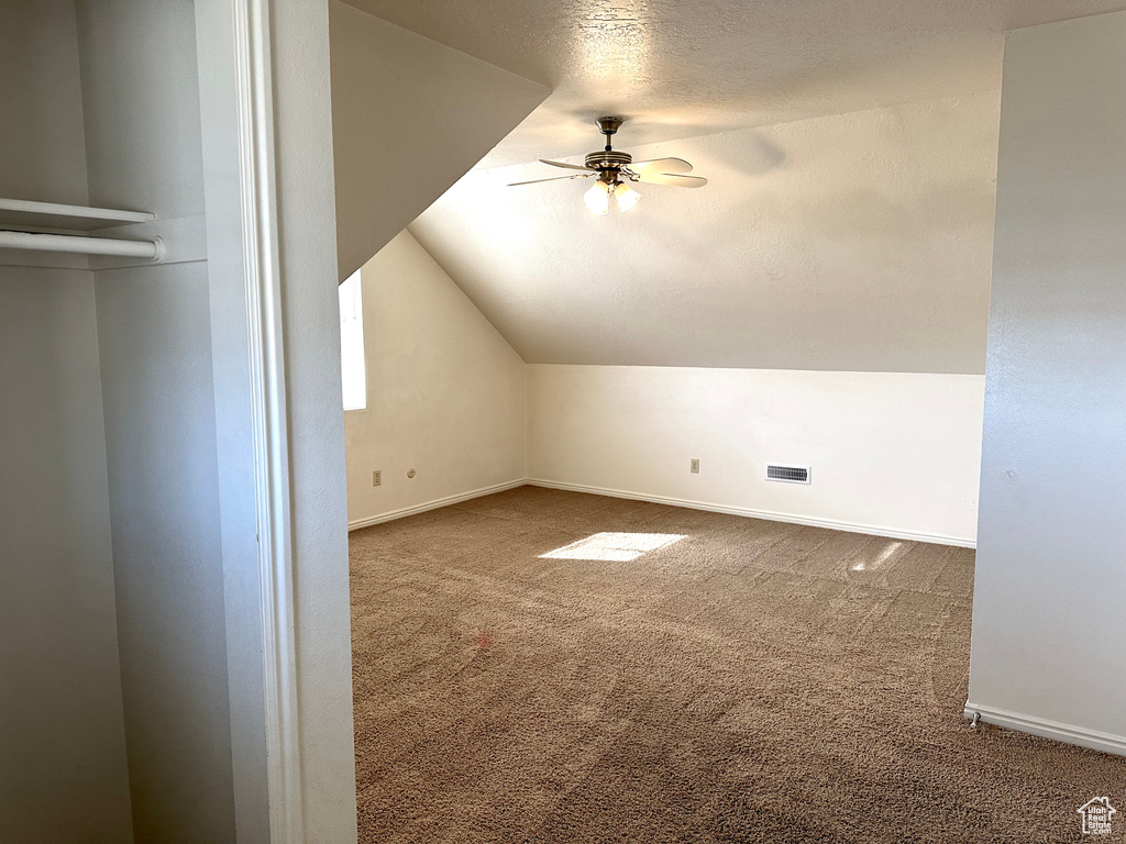 Additional living space with dark carpet, a textured ceiling, vaulted ceiling, and ceiling fan
