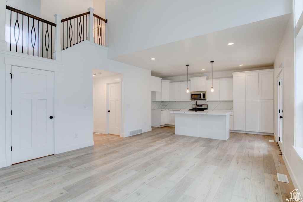 Kitchen with backsplash, stainless steel appliances, white cabinetry, and light hardwood / wood-style flooring
