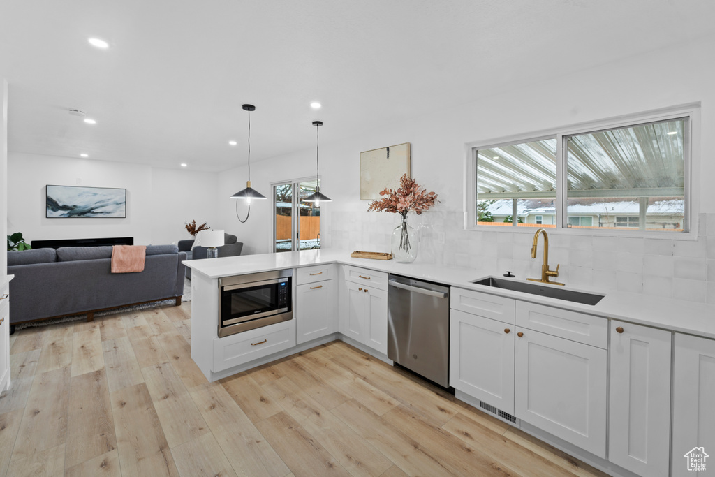 Kitchen featuring tasteful backsplash, sink, decorative light fixtures, light hardwood / wood-style flooring, and stainless steel appliances