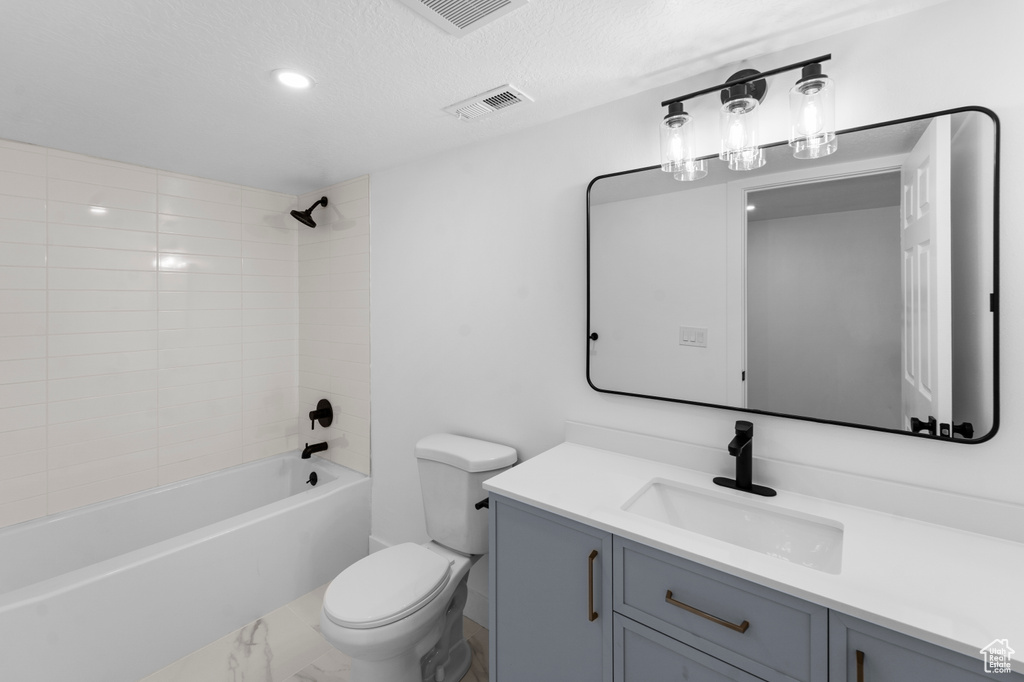 Full bathroom with a textured ceiling, tiled shower / bath, tile floors, vanity, and toilet